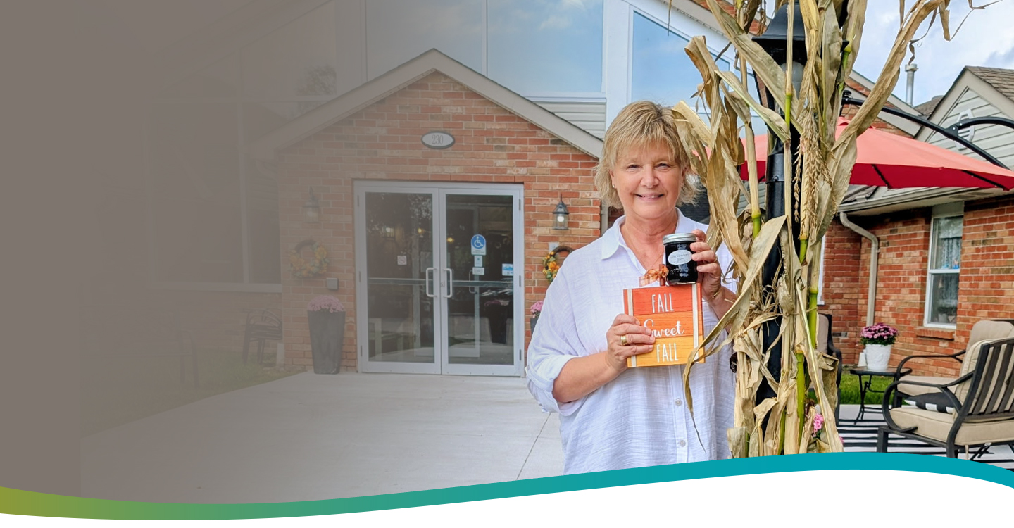 Lorree, General Manager at Atrium Retirement Residence in Orillia, standing outside the residence with a fall display, representing warmth and community spirit